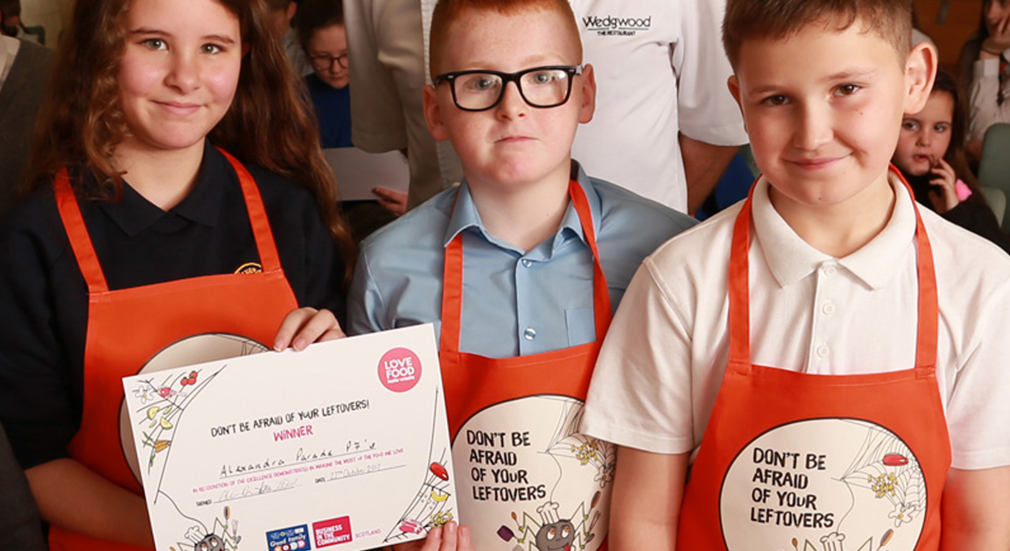 Two young children in red aprons holding a certificate