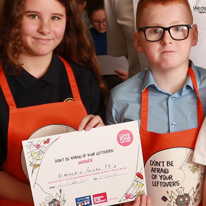 Two young children in red aprons holding a certificate