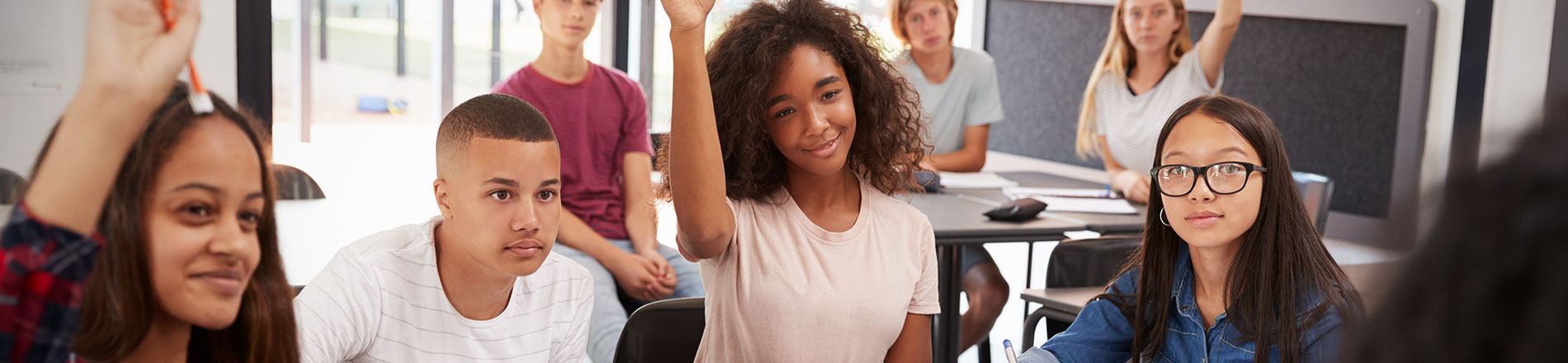 A young person holding their hand in the air in a classroom