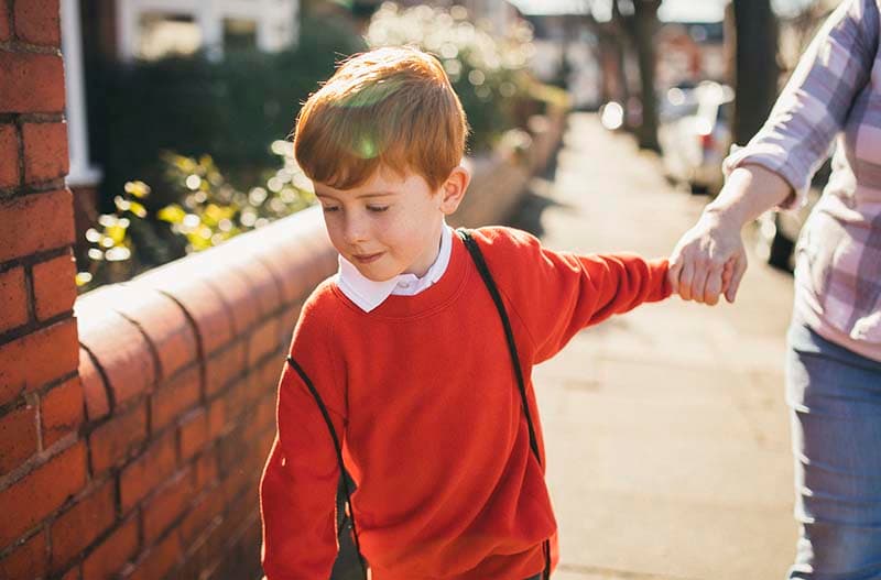 Photo of a boy wearing a red jumper holding his mum's hand walking back to school - signpost