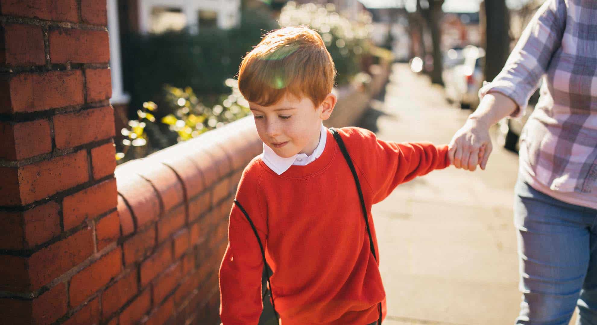 Photo of a boy wearing a red jumper holding his mum's hand walking back to school