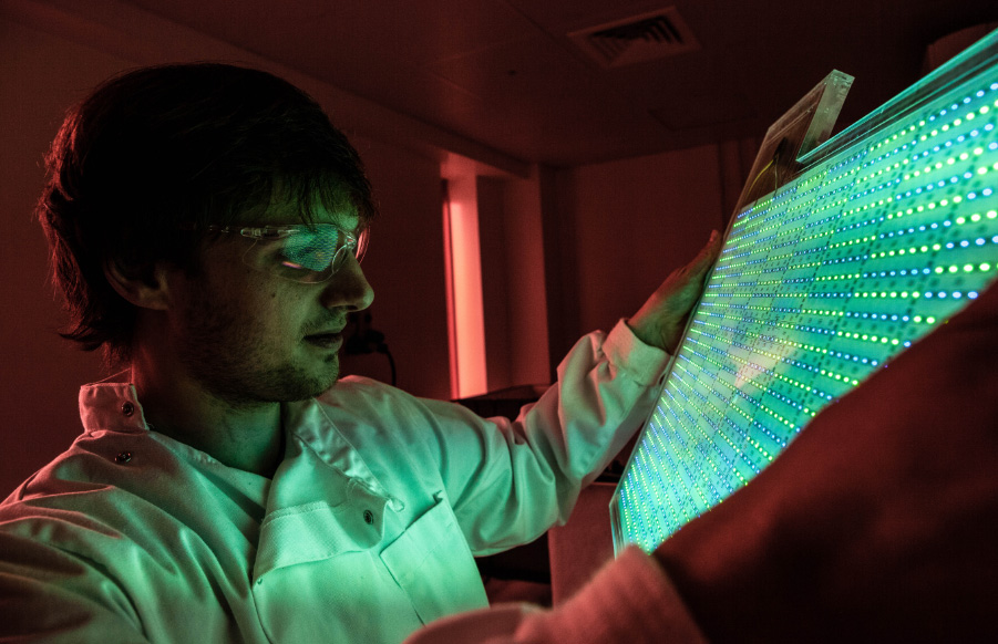 man holding panel in a dark room, panel glowing green 