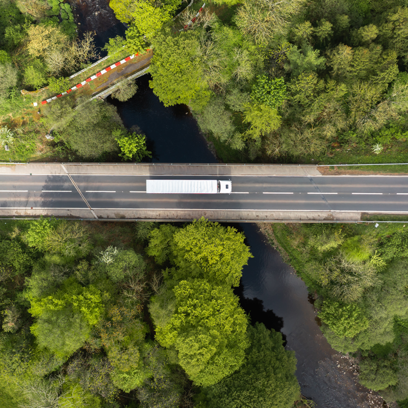 A high altitude shot looking down at a truck driving on a road through a forest