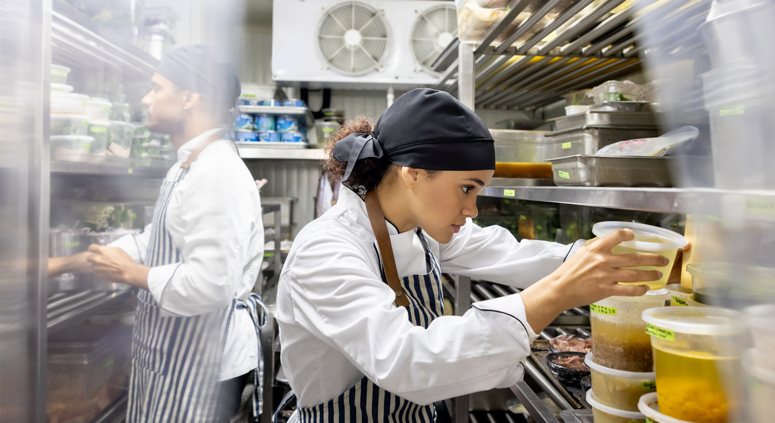 Two chefs in a cool storage area looking at food