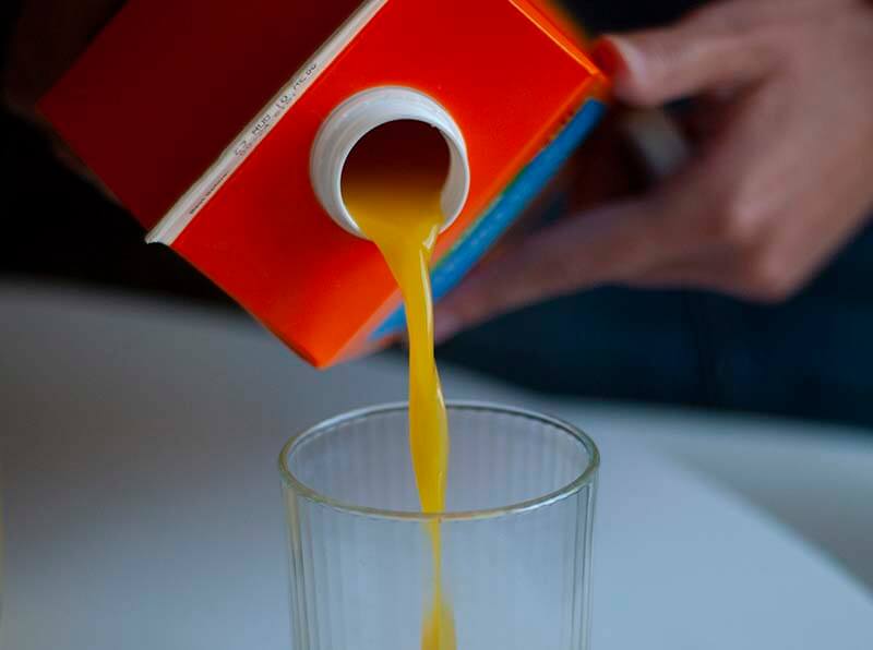 Person pouring orange juice from a drinks carton into a glass