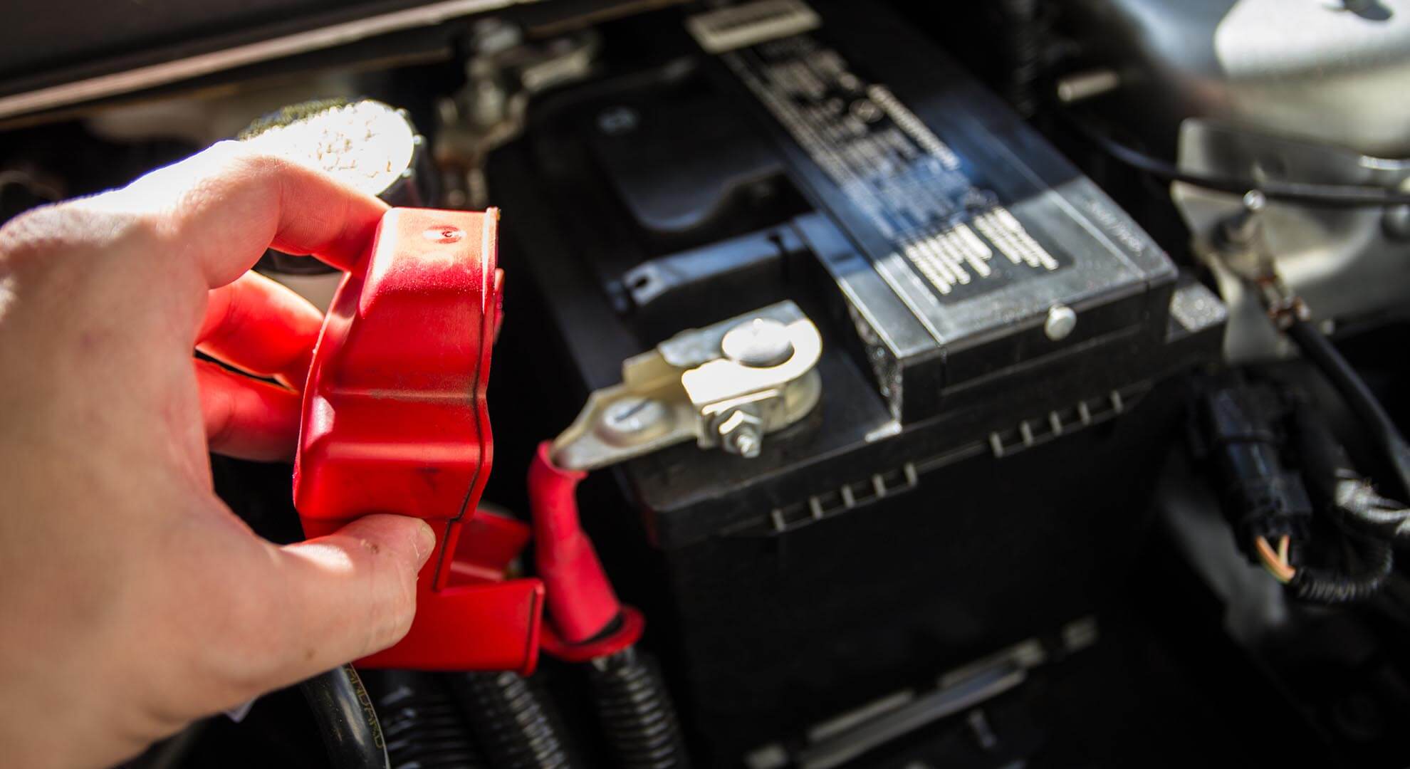 Person removing the red plastic cap on a car battery