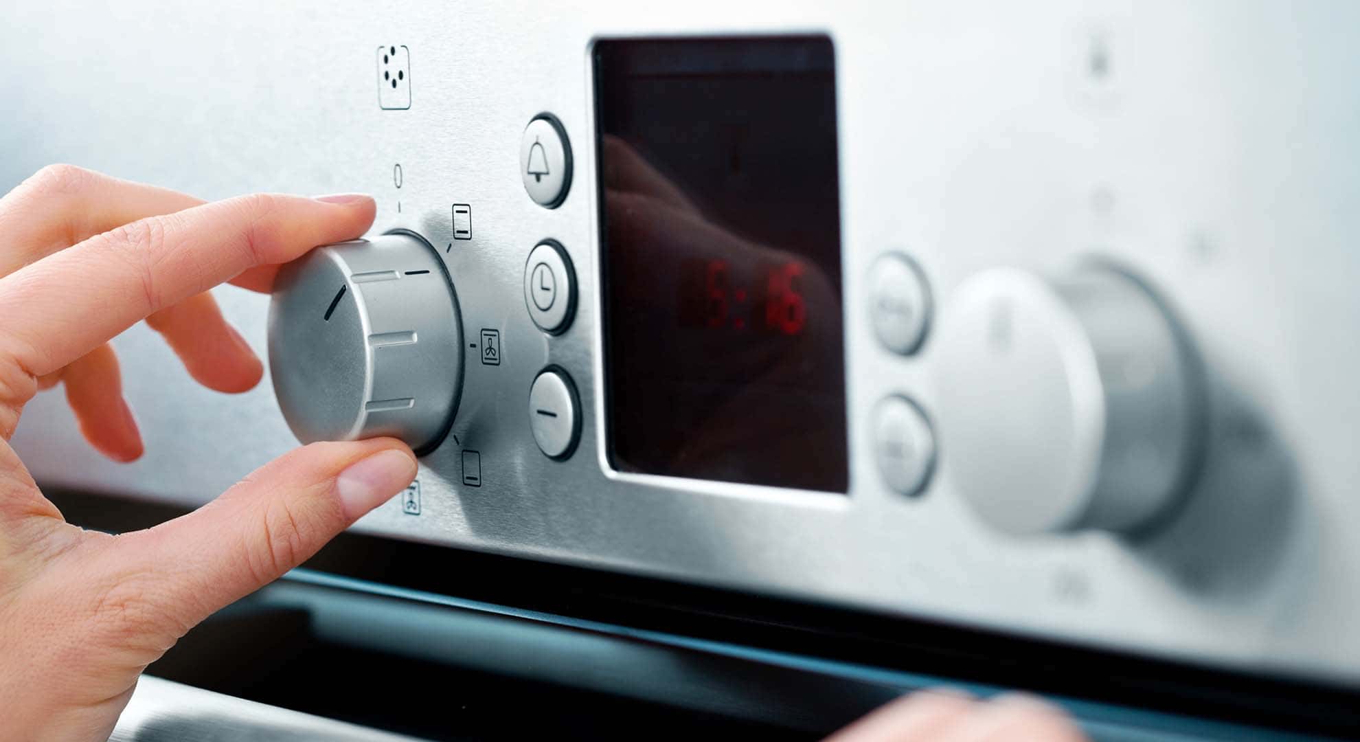 Photo of a person's hand turning the dial on an electric oven appliance
