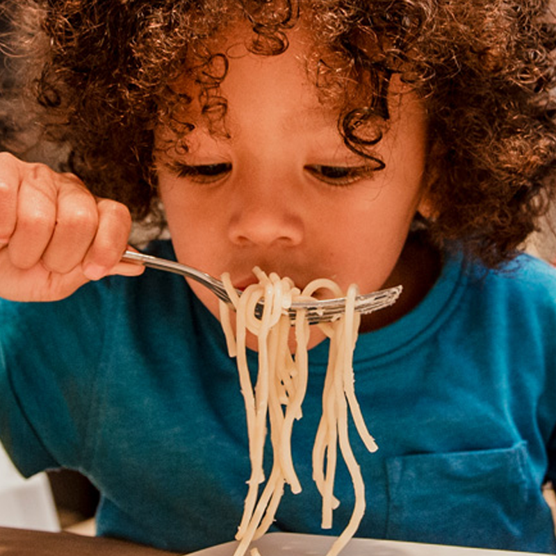 A young child eating a plate of spaghetti pasta