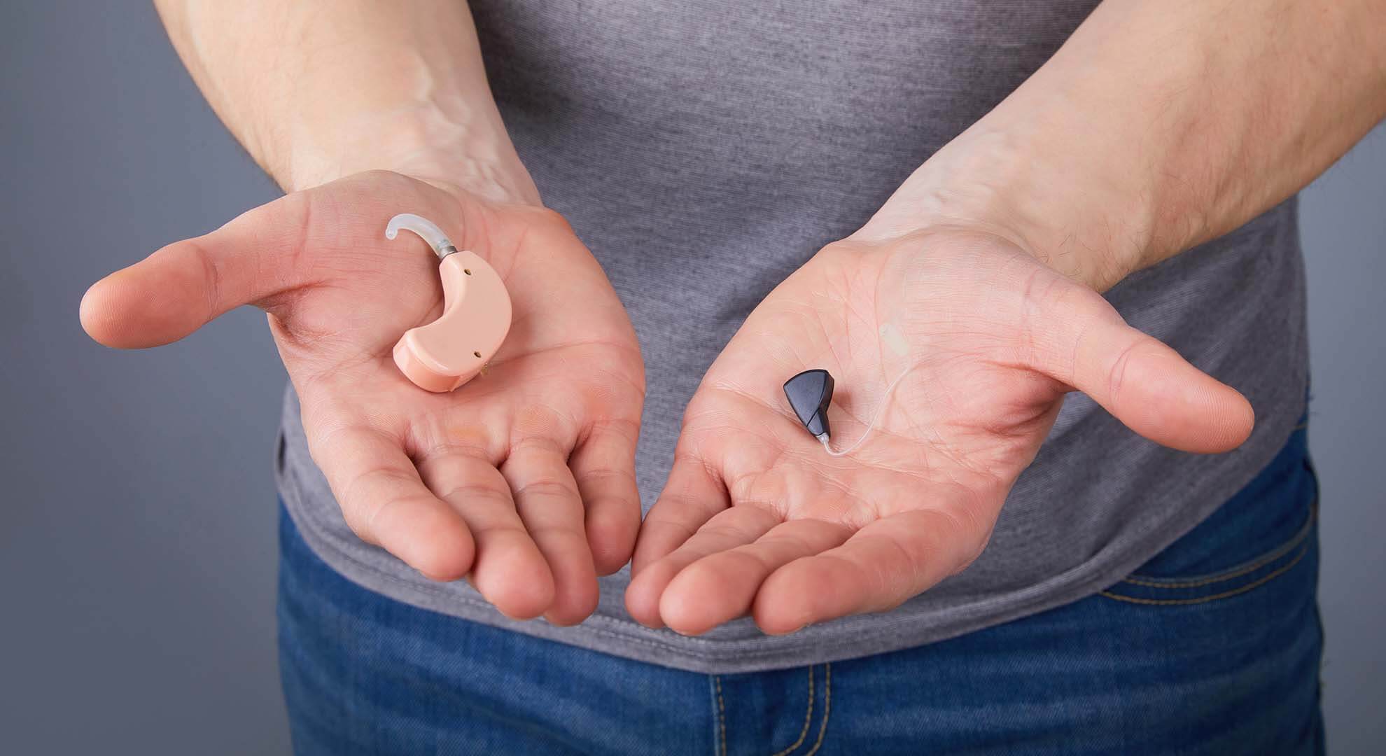 A person holding out different hearing aids on their hands