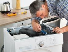A man is fixing a washing machine in a kitchen