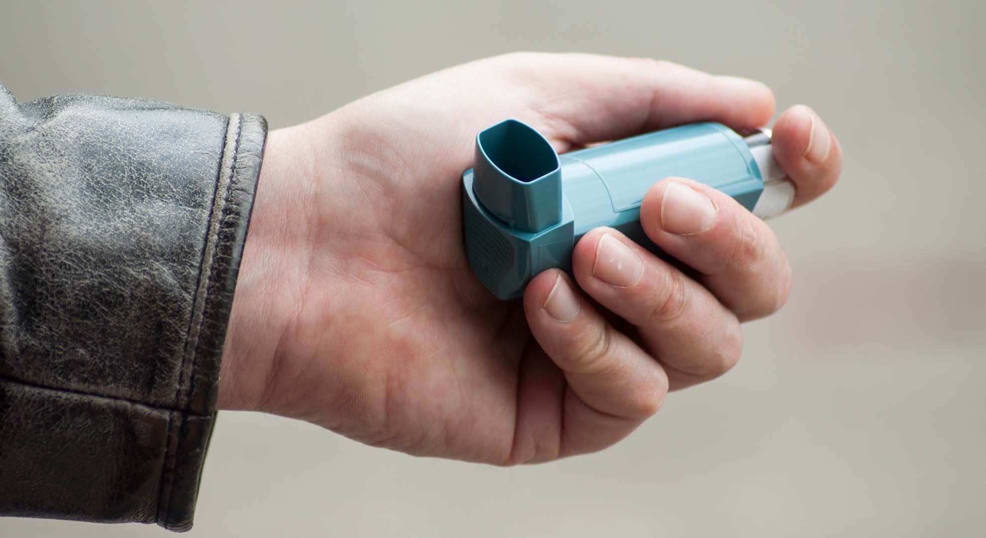 A person holding a blue inhaler in their hand