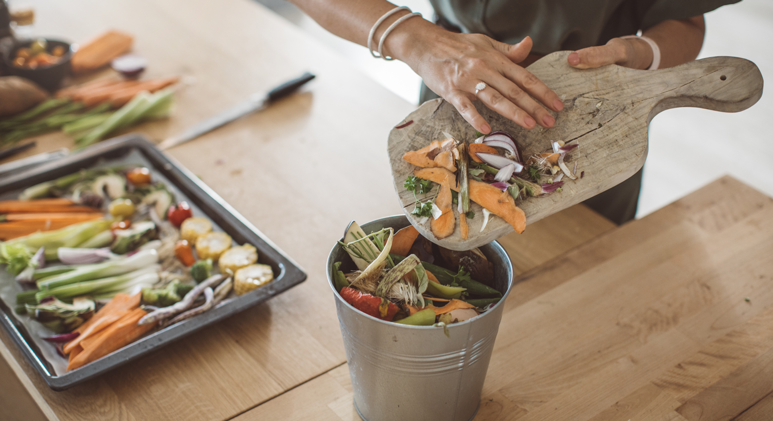 A persons hand pushing food waste from a chopping board into a food waste bin