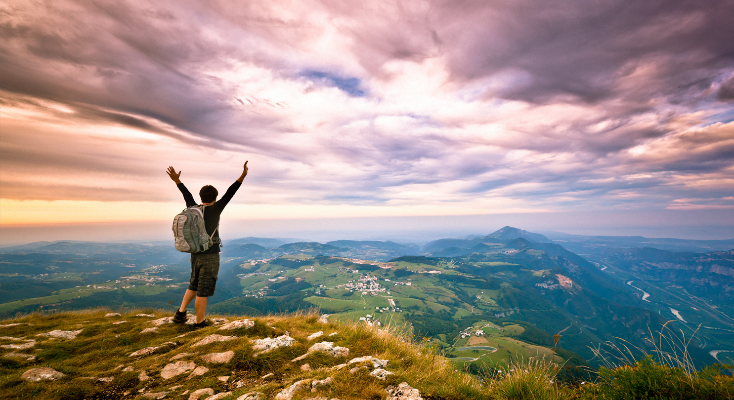 A person standing on top of a hill, looking into the distance with their arms up in the air