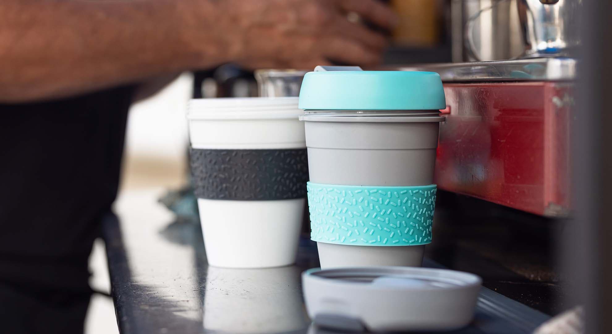 Photo of a barista making coffee in reusable cups in a cafe.