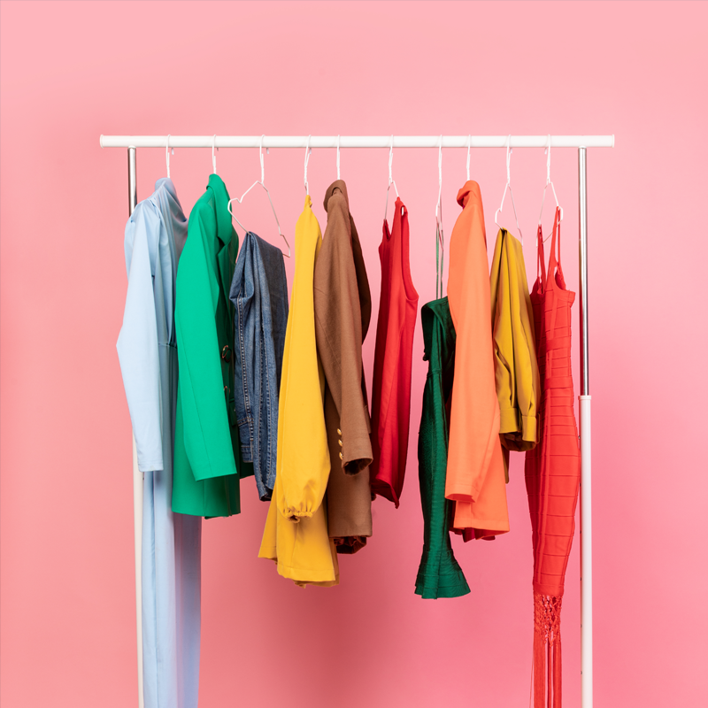 A rail of brightly coloured clothing in front of a pink background