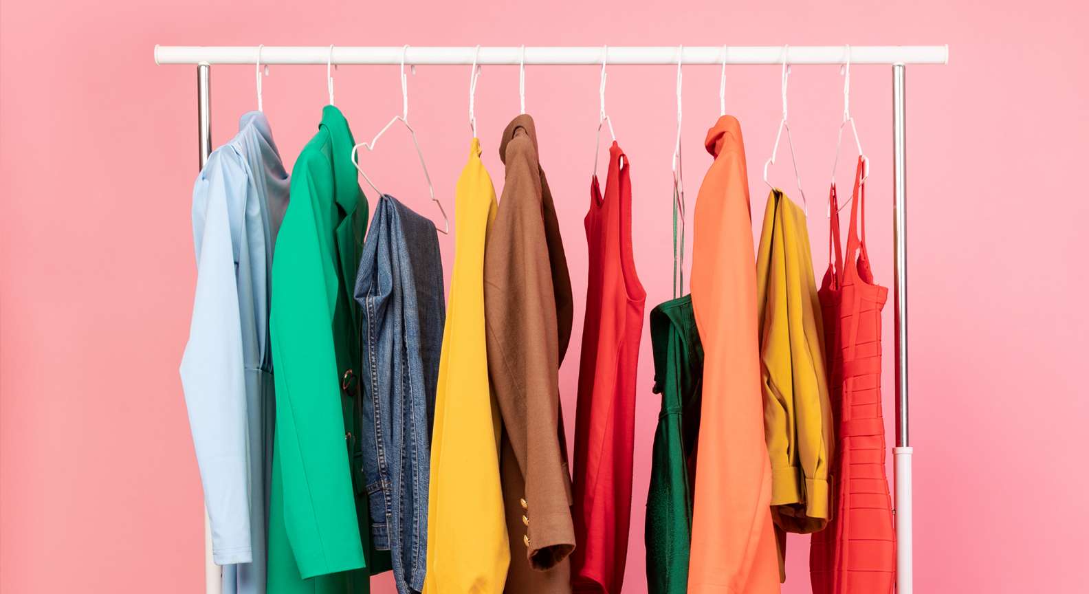 A rail of brightly coloured clothing in front of a pink background