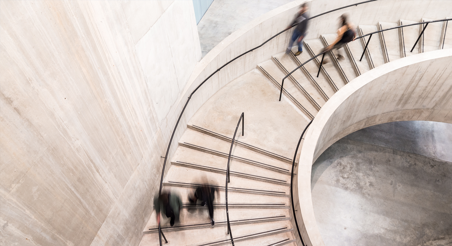 People walking down a spiral, circular staircase in a modern office building
