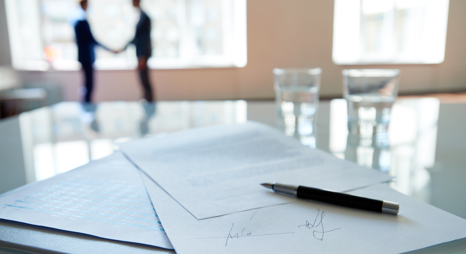 A signed contract, with two people shaking hands in the background