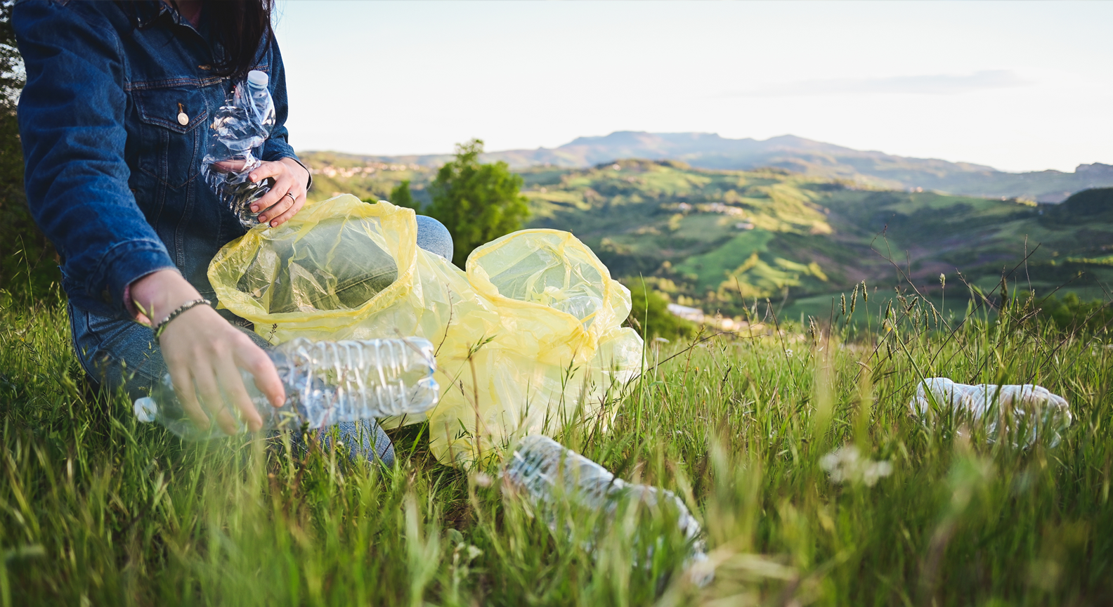 A person picking littered plastic bottles on a grassy hill