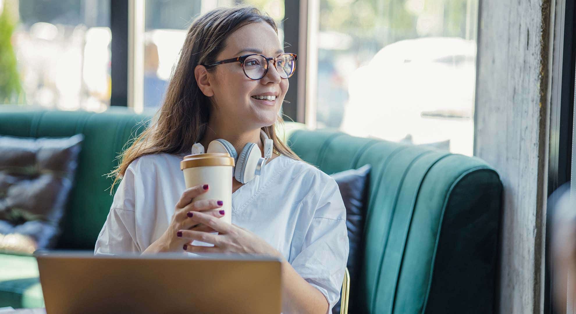 Photo of a person with a reusable coffee cup sitting in front of a laptop