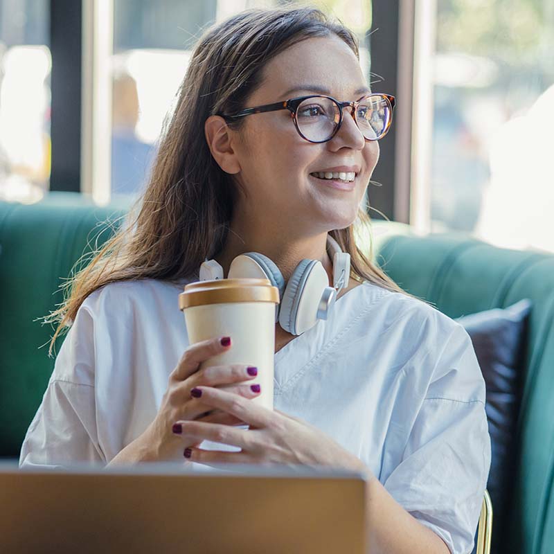 Photo of a person with a reusable coffee cup sitting in front of a laptop