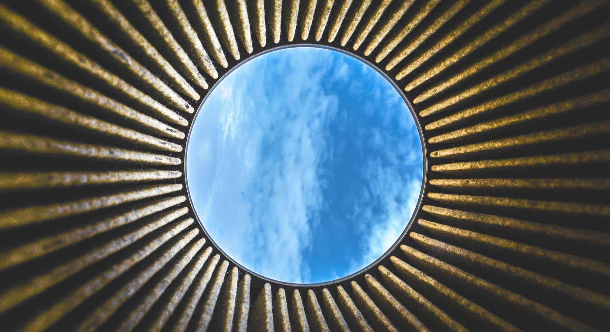 Photo of looking up through a circle of dark corrugated metal towards blue sky with whispy clouds