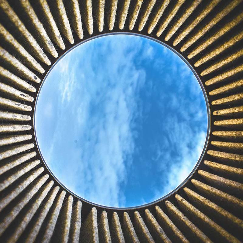 Photo of looking up through a circle of dark corrugated metal towards blue sky with whispy clouds