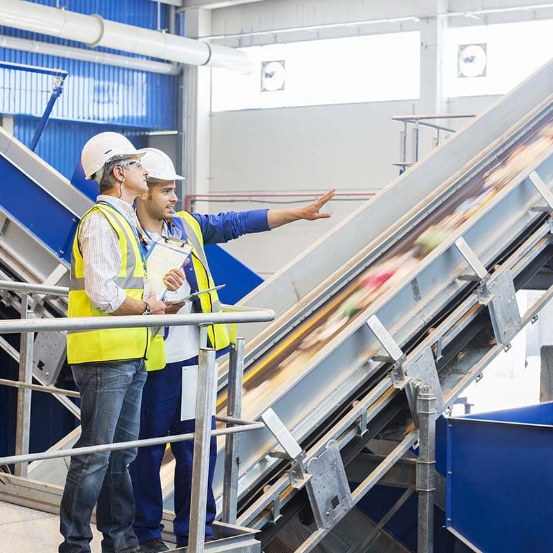 Photo of two people in high viz jackets and hard hats beside a conveyor belt with recylable materials