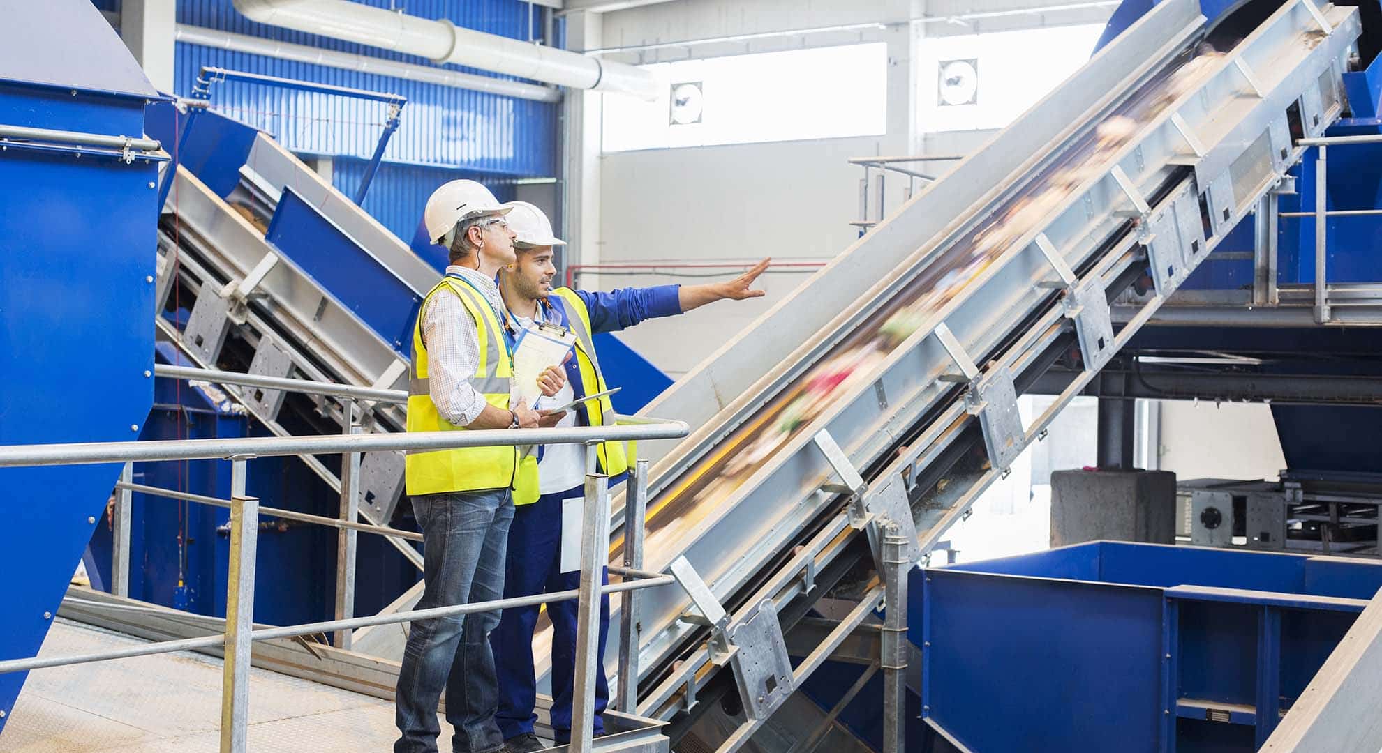 Photo of two people in high viz jackets and hard hats beside a conveyor belt with recylable materials