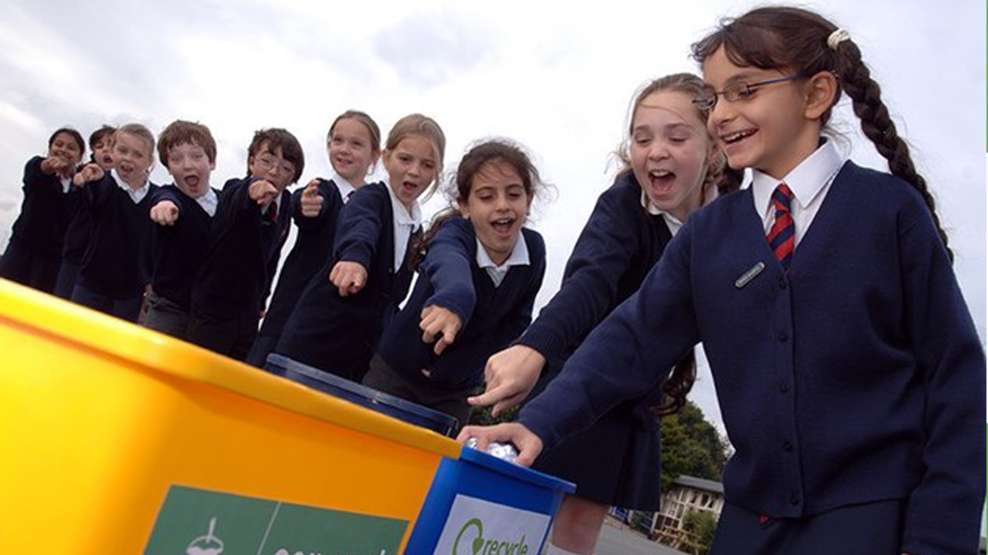 A group of school children standing over and pointing to a recycling bin