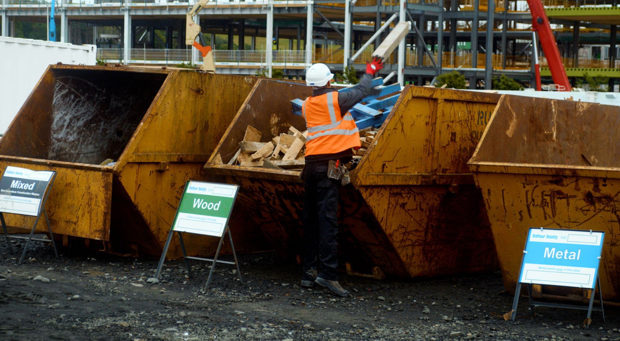 Worker sorting construction waste into designated material skips