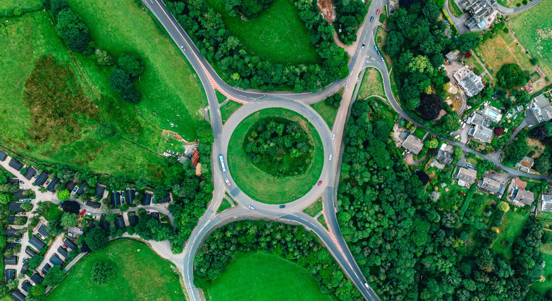 Aerial view photo of a circular roundabout surrounded by green fields trees and houses