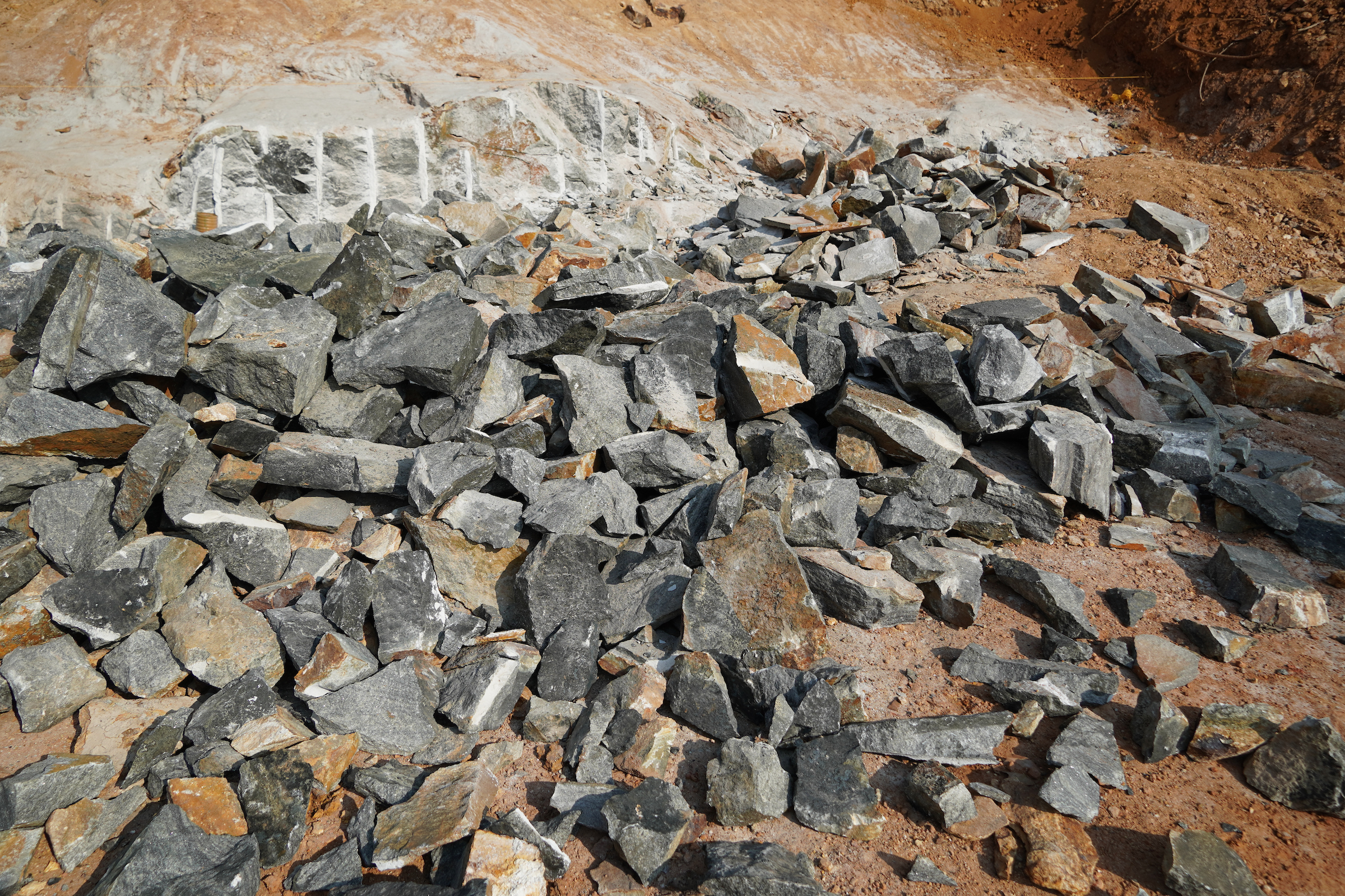 A pile of mined rocks with a deforested scene in the background