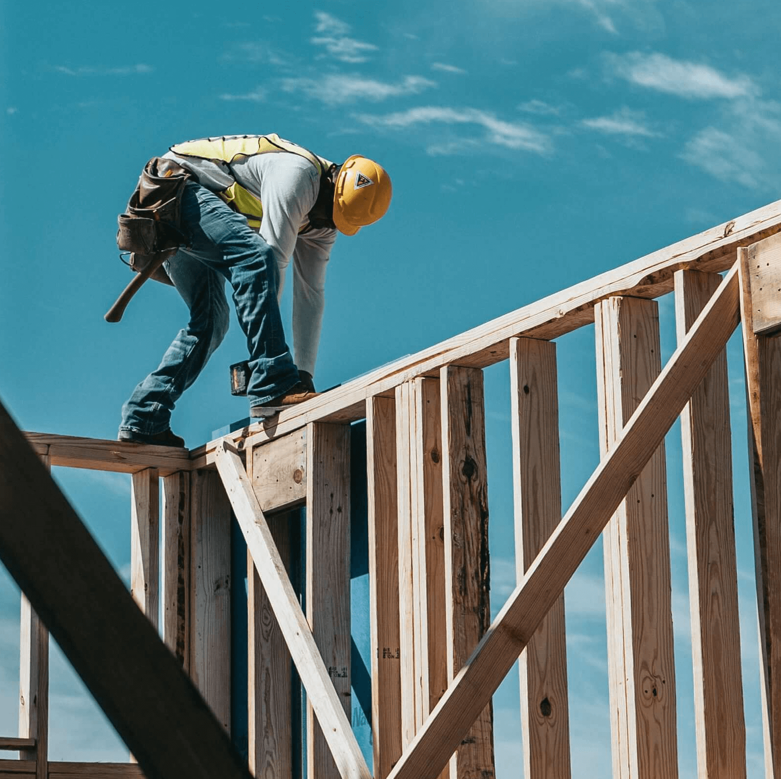 A construction worker stands atop a wooden house frame