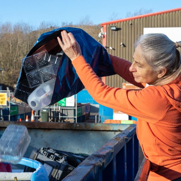 Person using HWRC tipping bag of recyclables into container