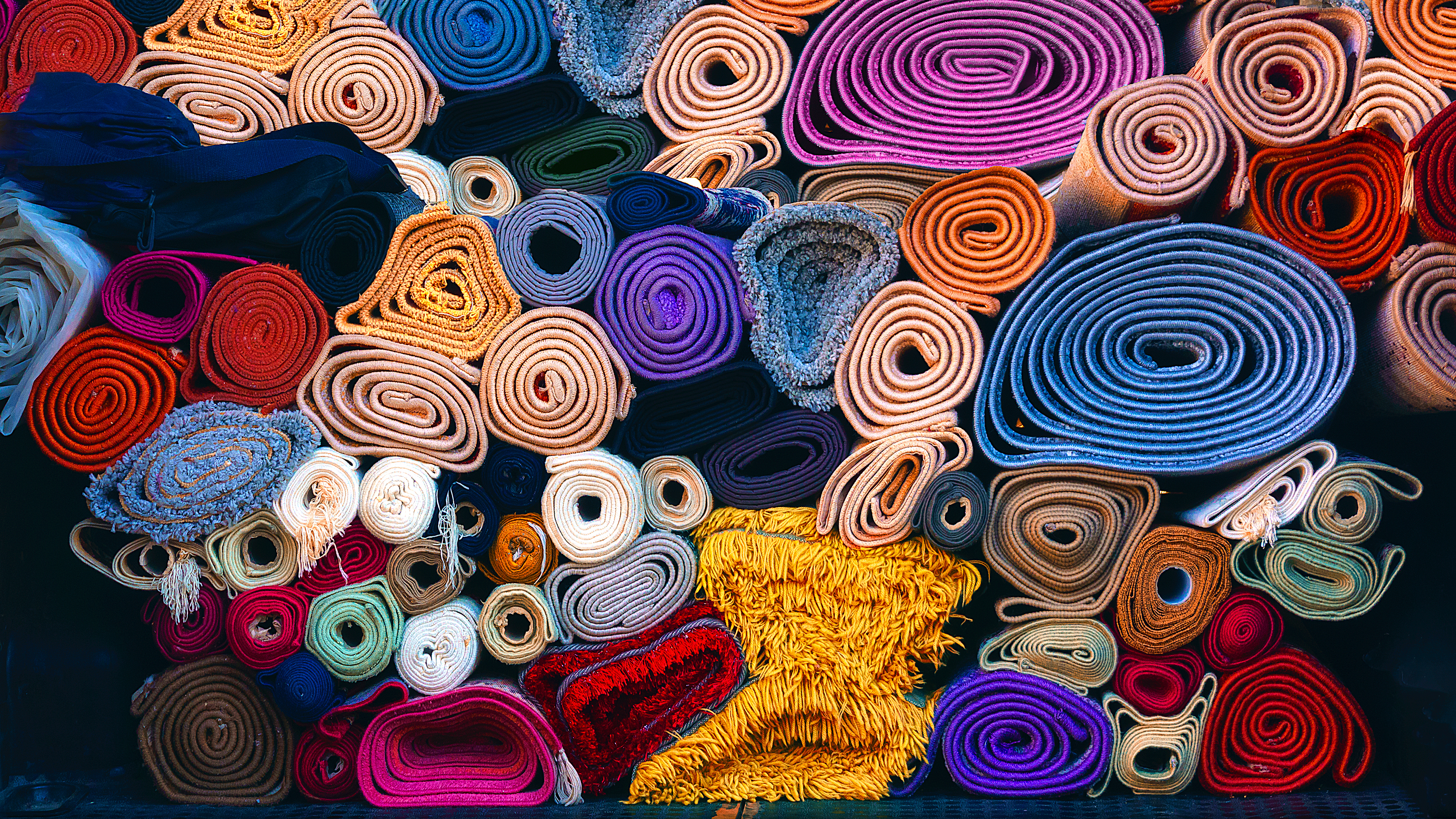 Colourful rolls of fabric stacked closely together, showing various textures and shades.
