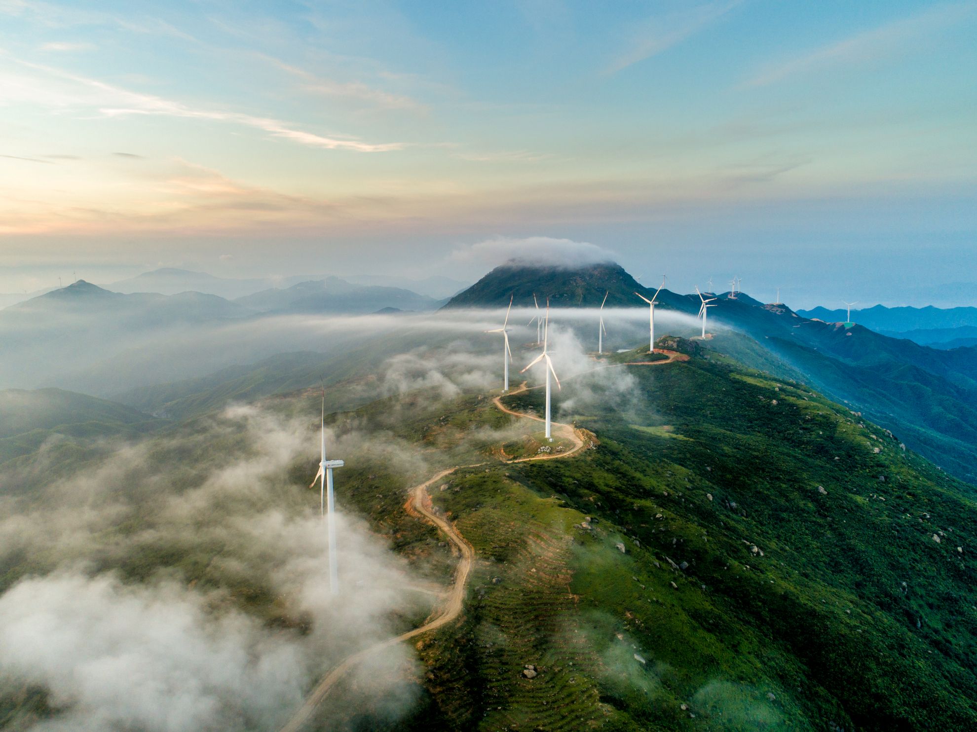 A row of wind turbines along a misty mountain ridge at sunrise.