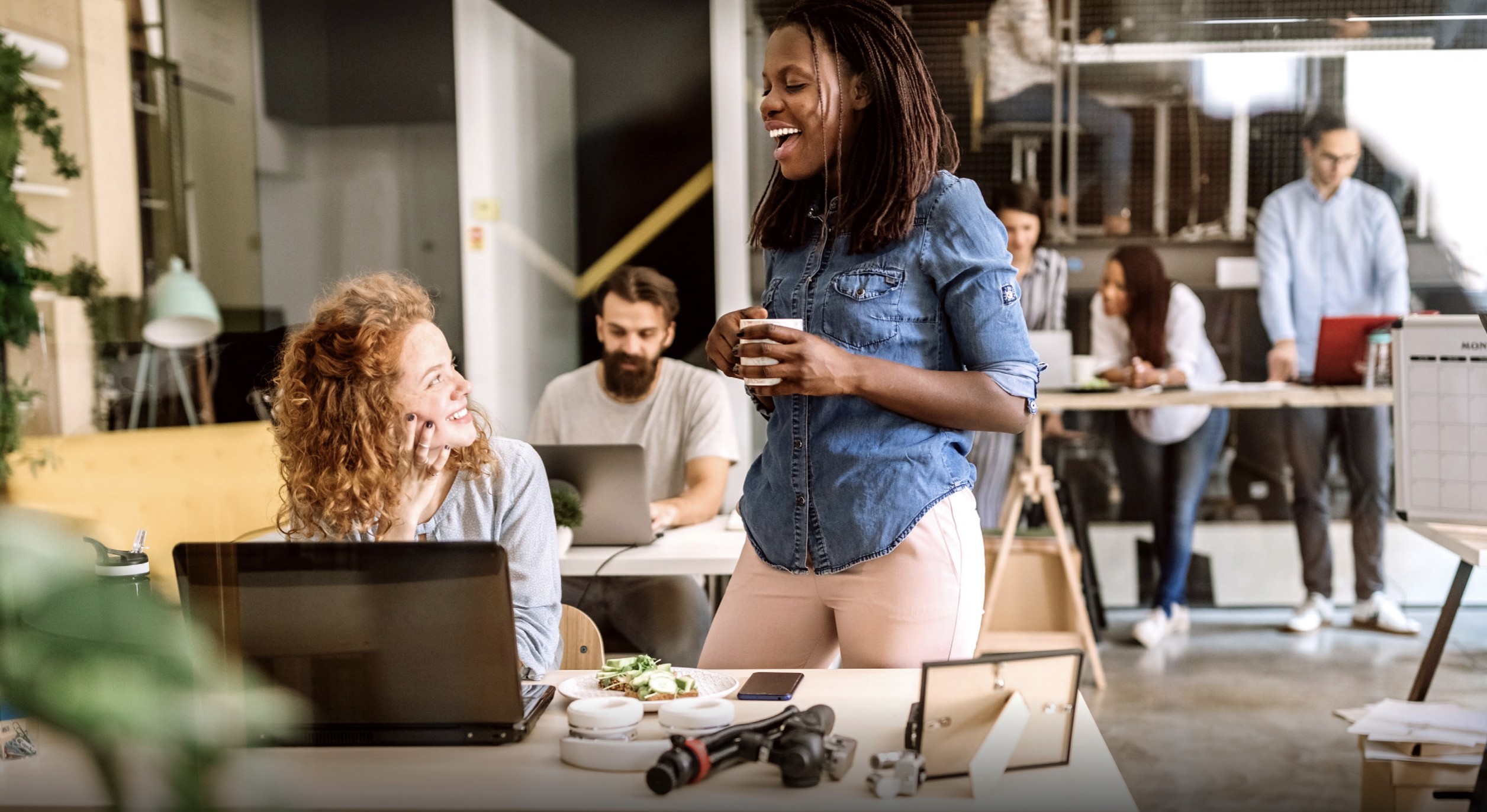 women speaking, one sat ad the other standing, both smiling 