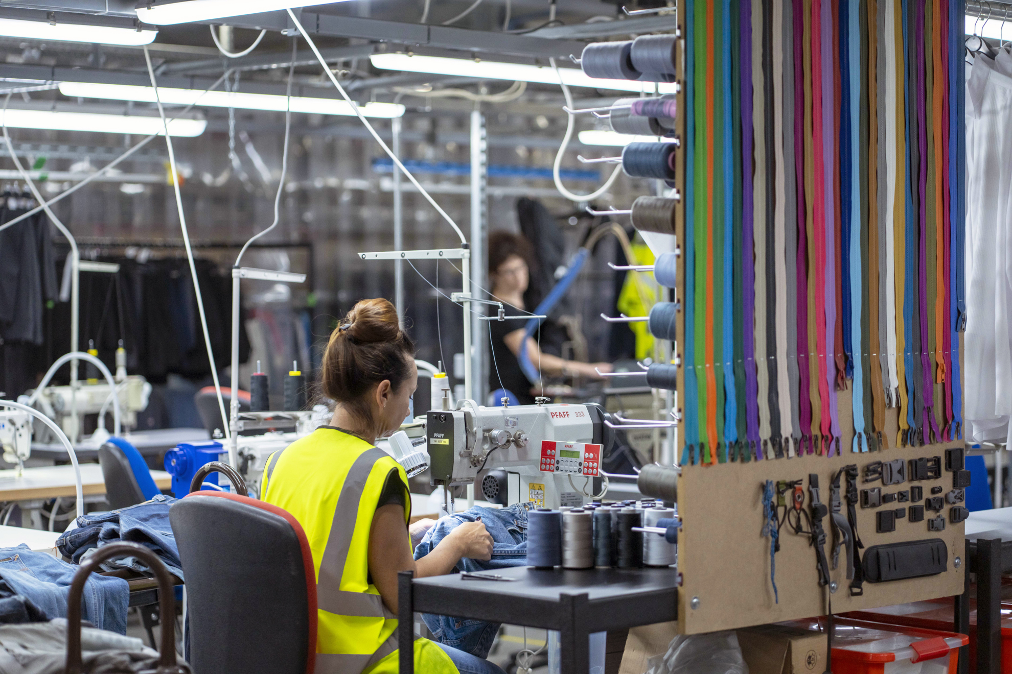 ACS Clothing industrial factory with female worker in a high-visibility jacket sewing garmets