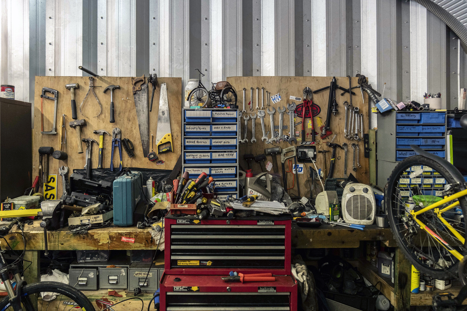Wall-mounted tool board with various hand tools above a cluttered workbench in a bike repair shop.