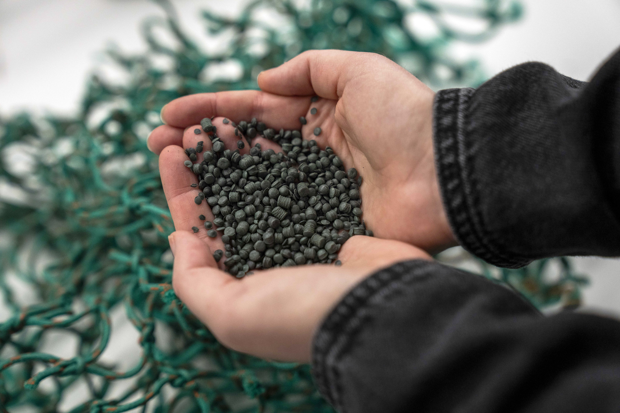 hands cupping recycled plastic pellets over fishing netting