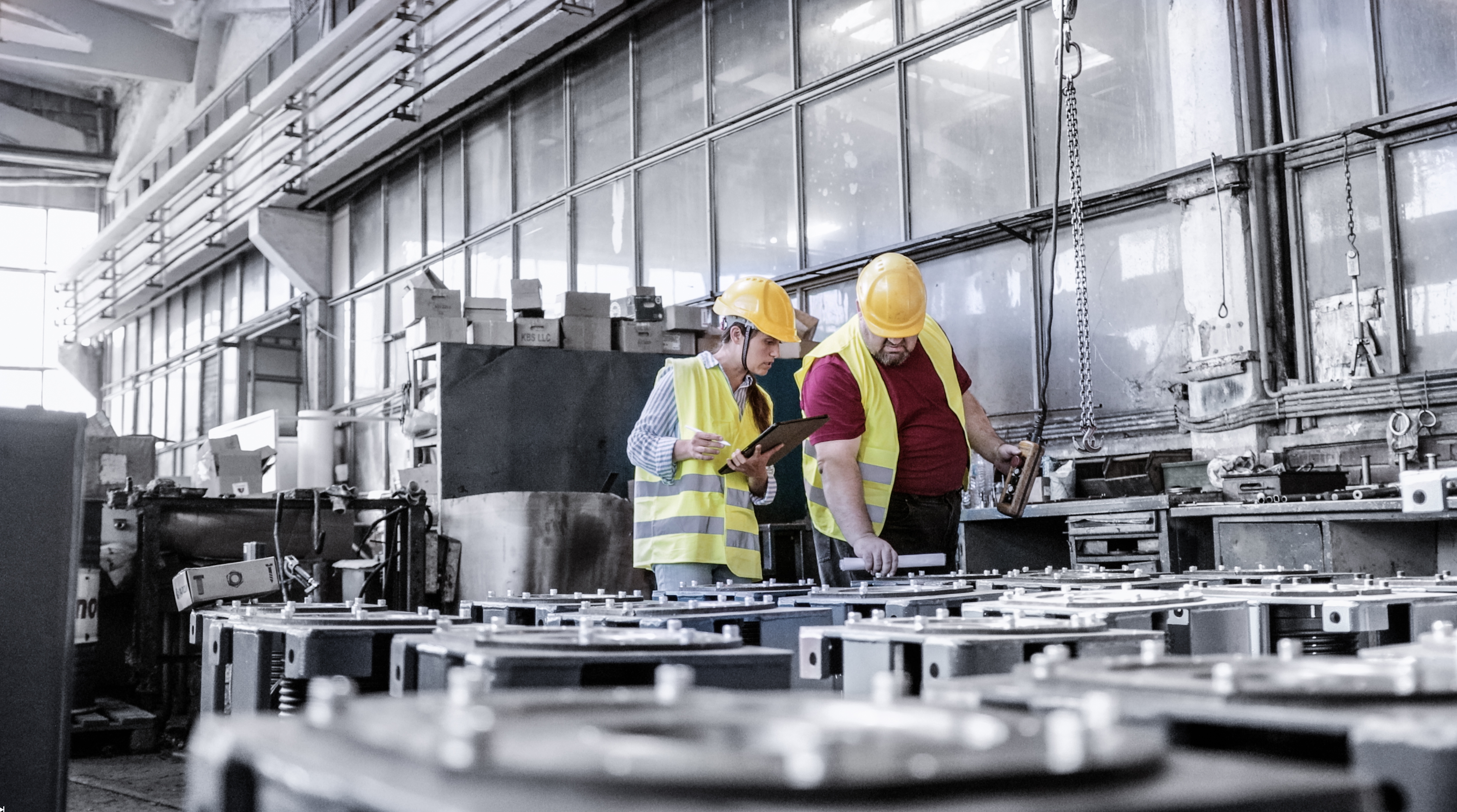 Workers in safety vests and hard hats inspecting machinery inside an industrial workshop.