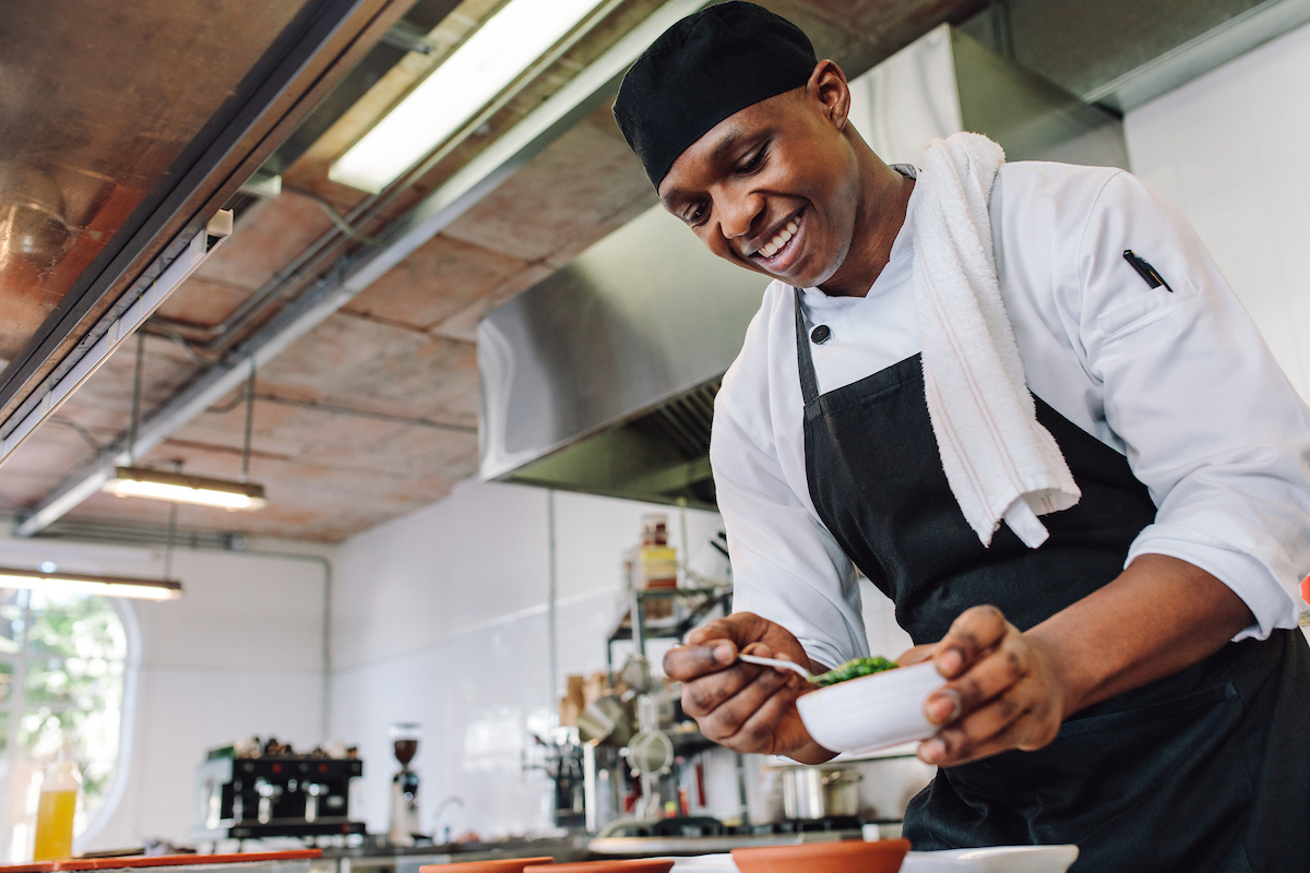 Chef in a commercial kitchen preparing food in a white bowl.