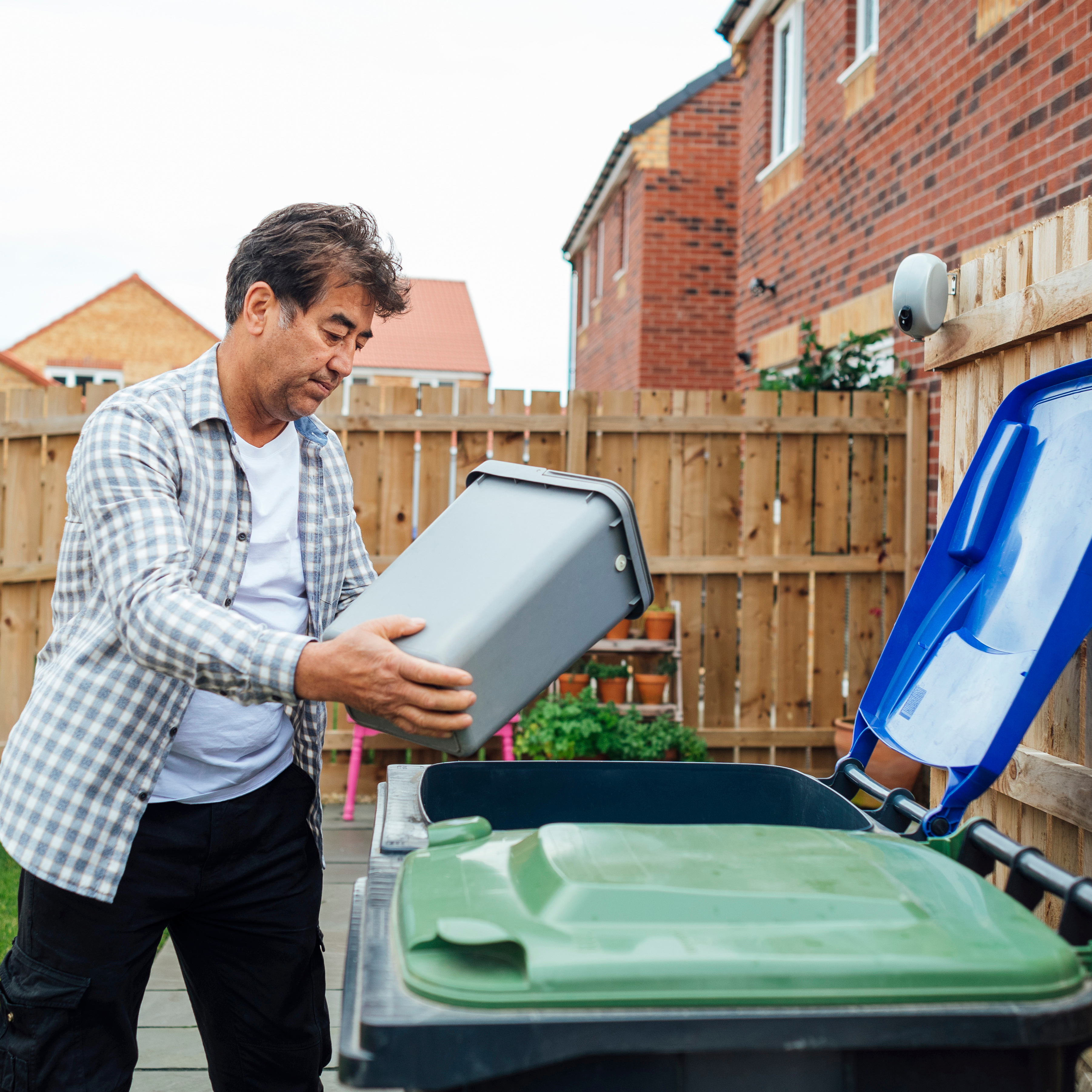 A man emptying a small household bin into a larger household waste wheelie bin