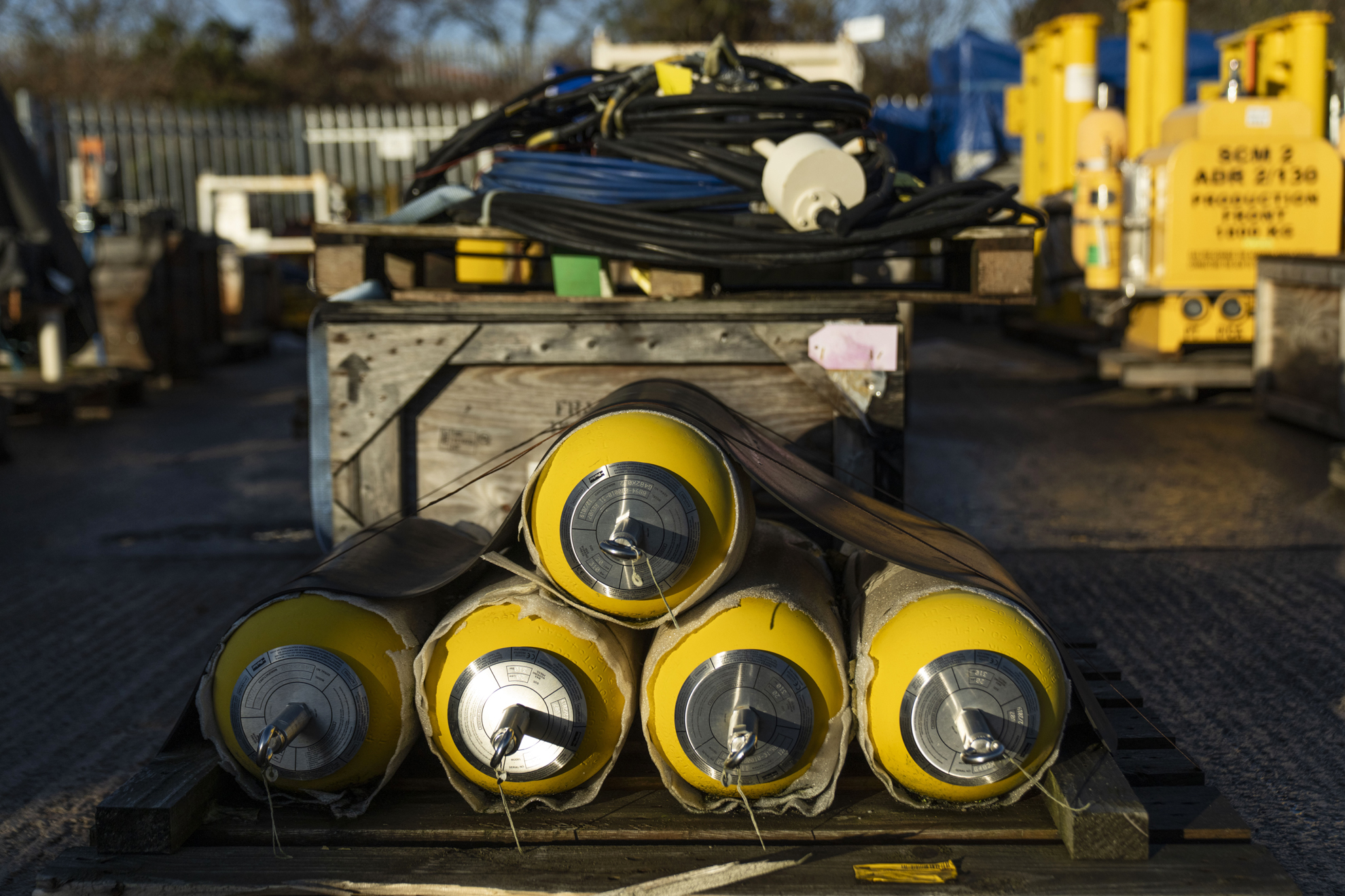 Stack of yellow subsea equipment strapped to pallet in outdoor warehouse facility 