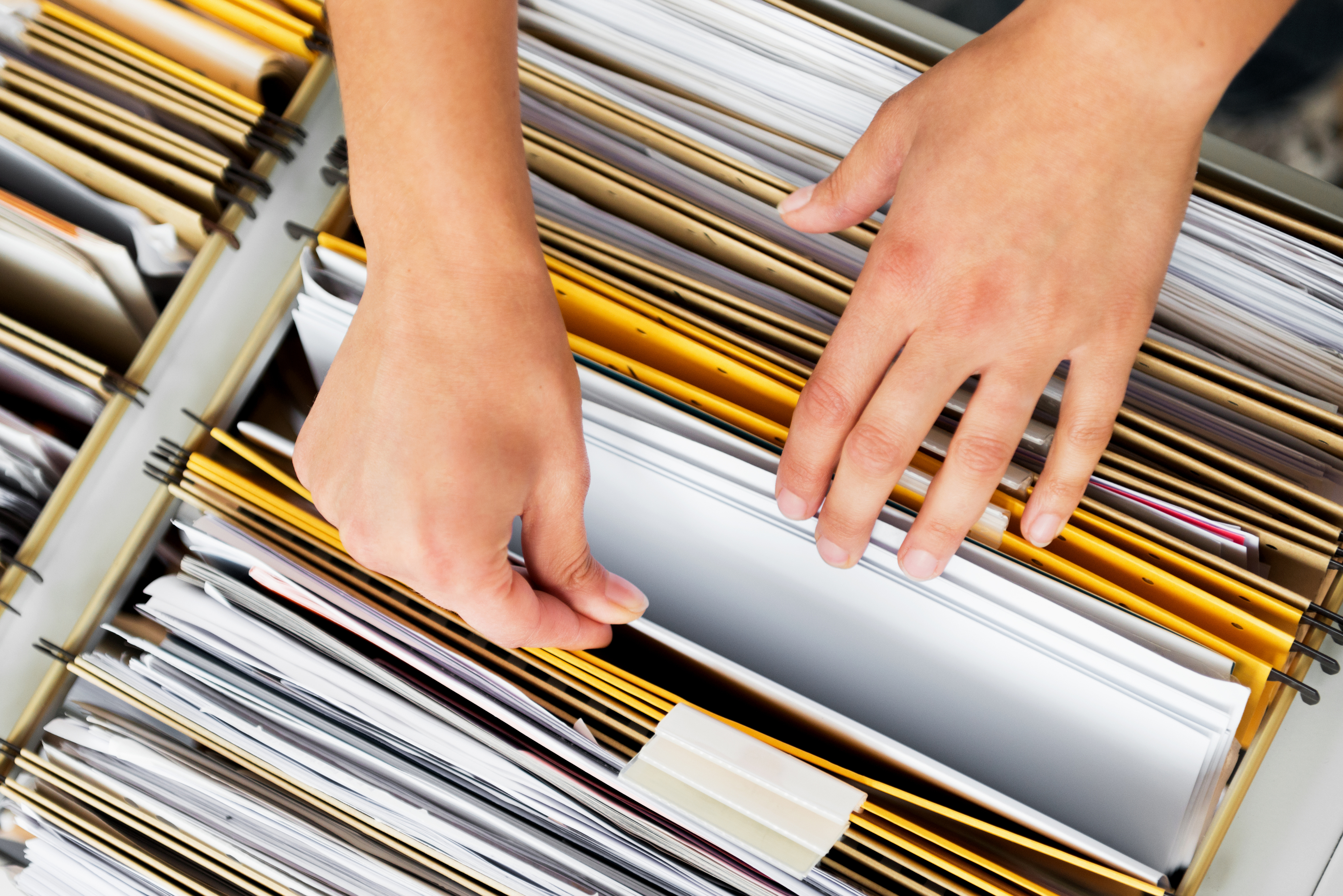 Hands sorting through organised folders and documents in a filing cabinet