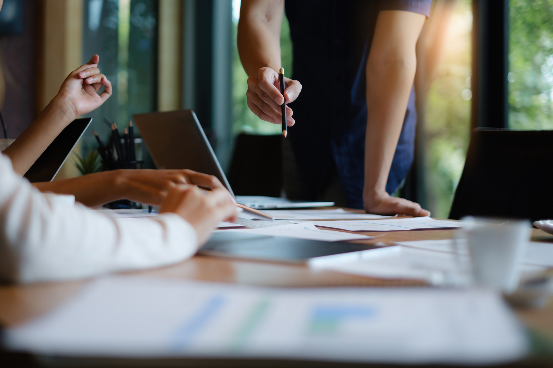 People gathered around a table, pointing at documents and working on laptops during a meeting.