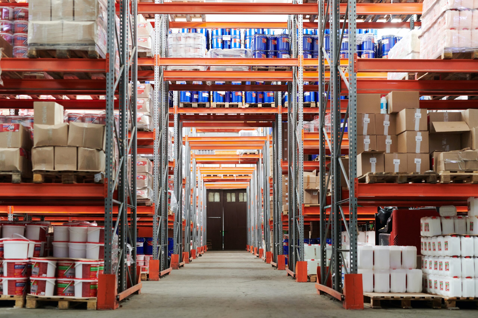Warehouse aisle with tall storage racks stacked with boxes and containers.