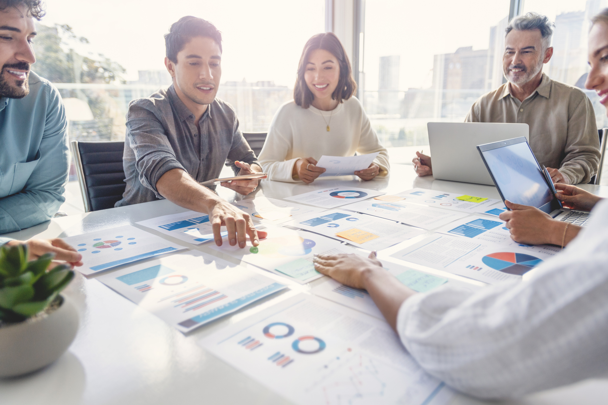 People collaborating around a conference table, reviewing printed charts and reports during a business meeting.