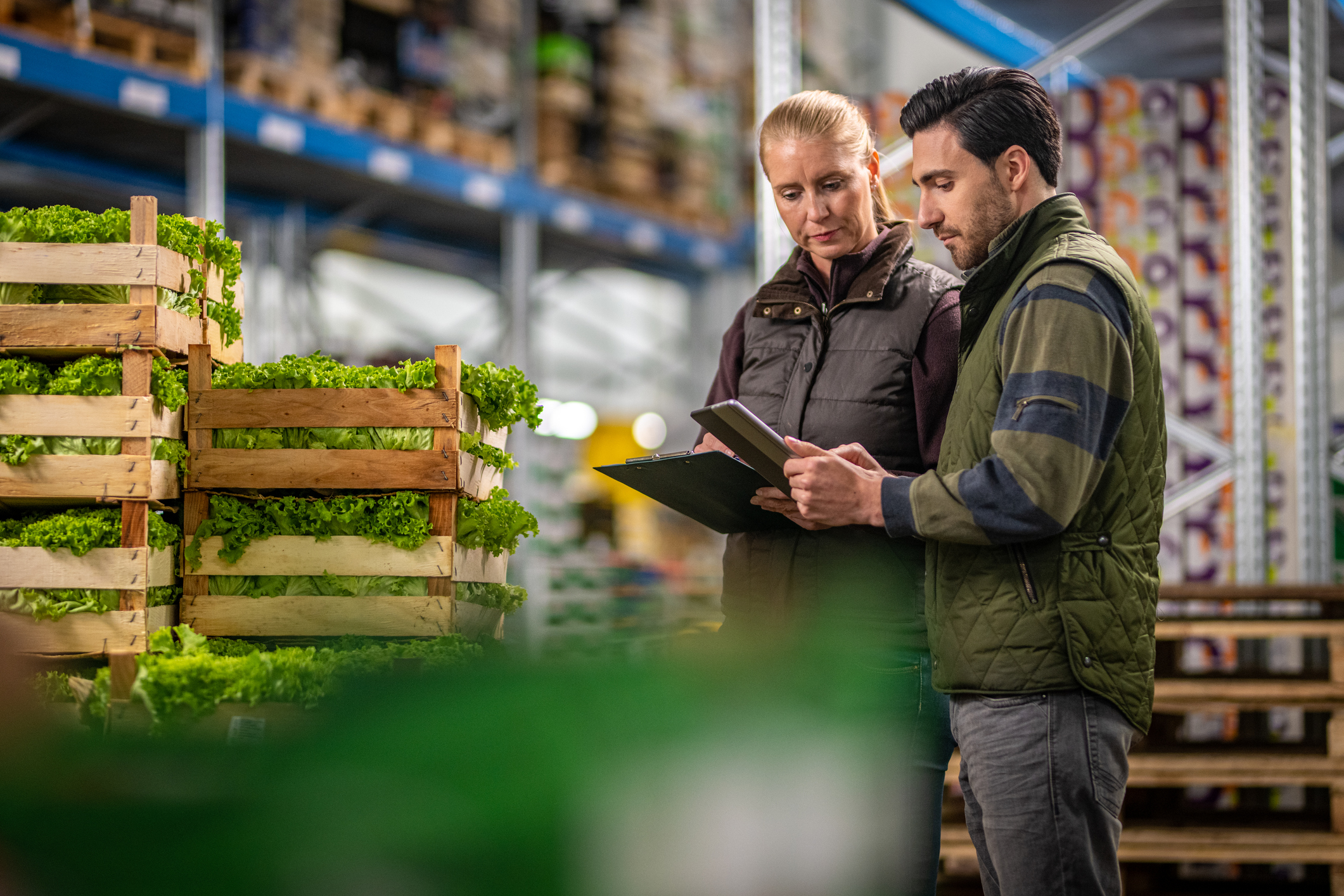 Workers checking inventory and stock data in a warehouse beside crates of fresh produce.